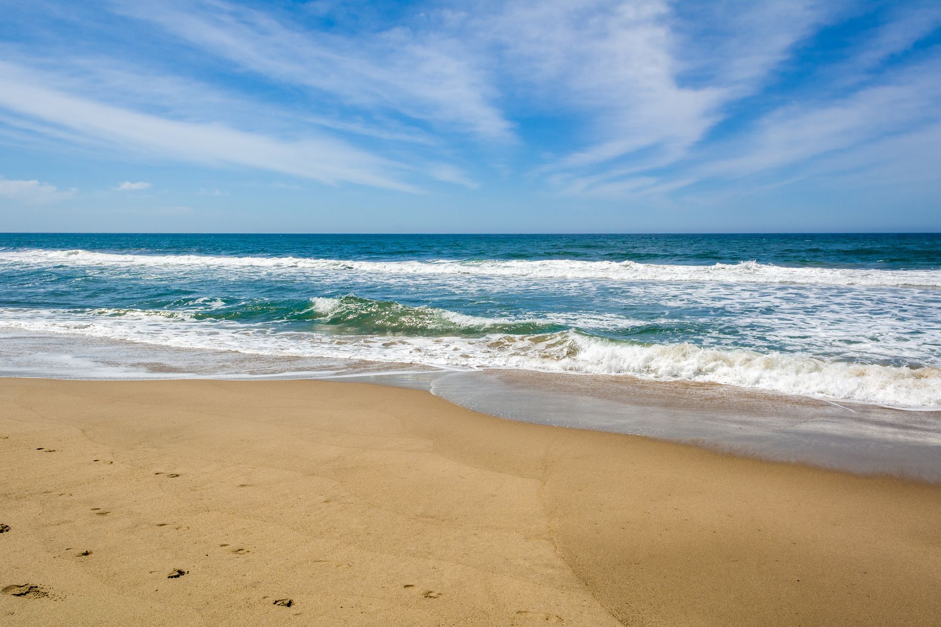 A sandy beach with waves crashing against the shore on a sunny day.