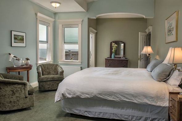 A bedroom with a king size bed , chairs , dresser and mirror.