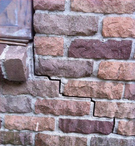 Cracked brick wall, mortar damage with displaced brick. Various colors of brick.