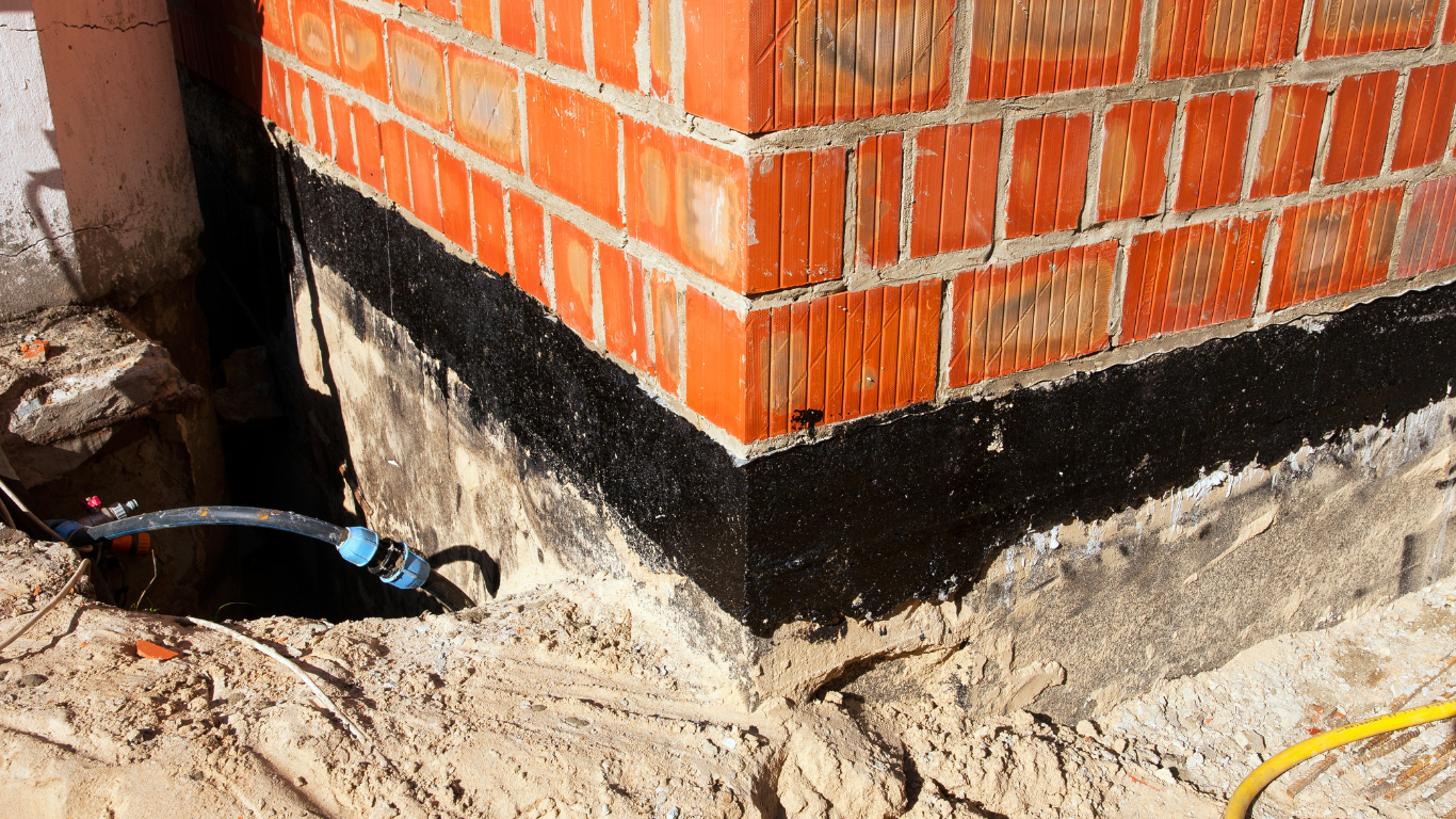 Brick building corner with black waterproof coating on the foundation, surrounded by sand.