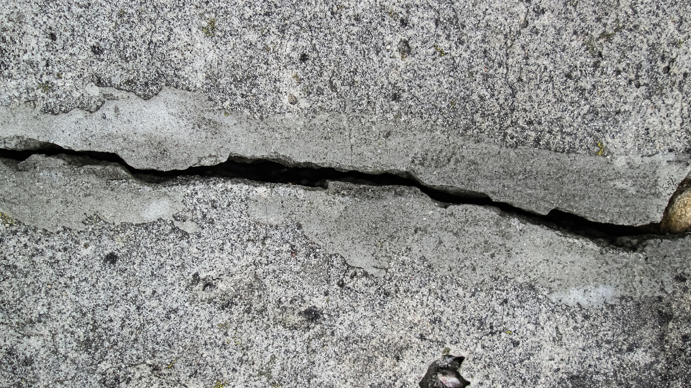 Close-up of a cracked, gray concrete surface with dark fissure.