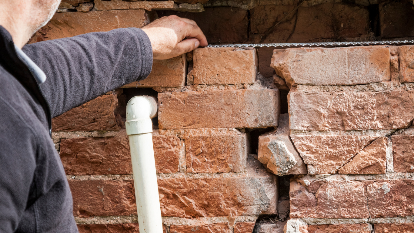 Man inspecting a cracked brick wall with a white pipe.