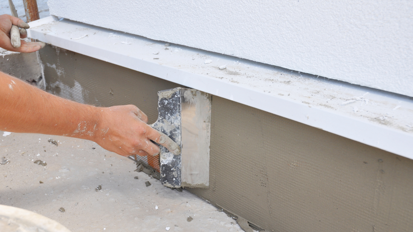 Person applying stucco with a trowel to the foundation of a building.