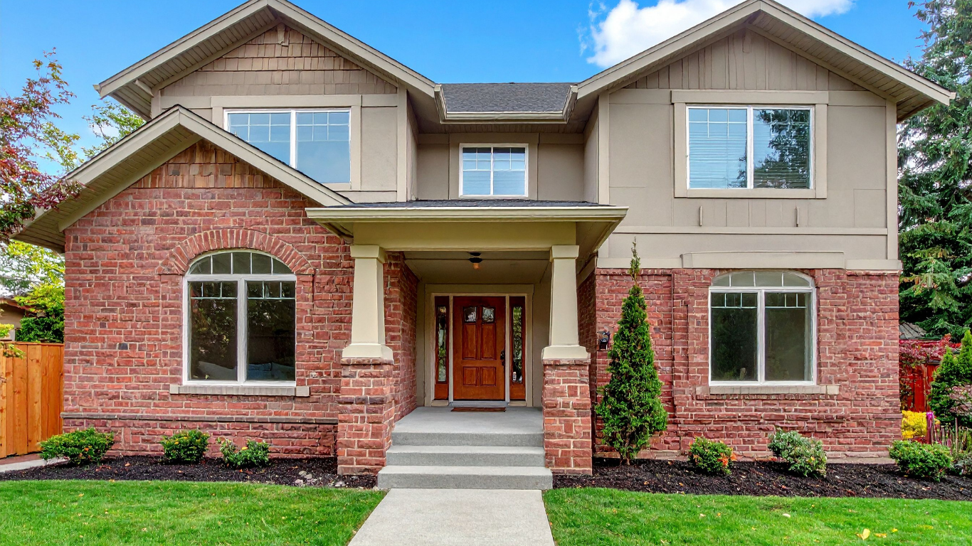 Two-story house with red brick facade, beige siding, and a front porch with steps.