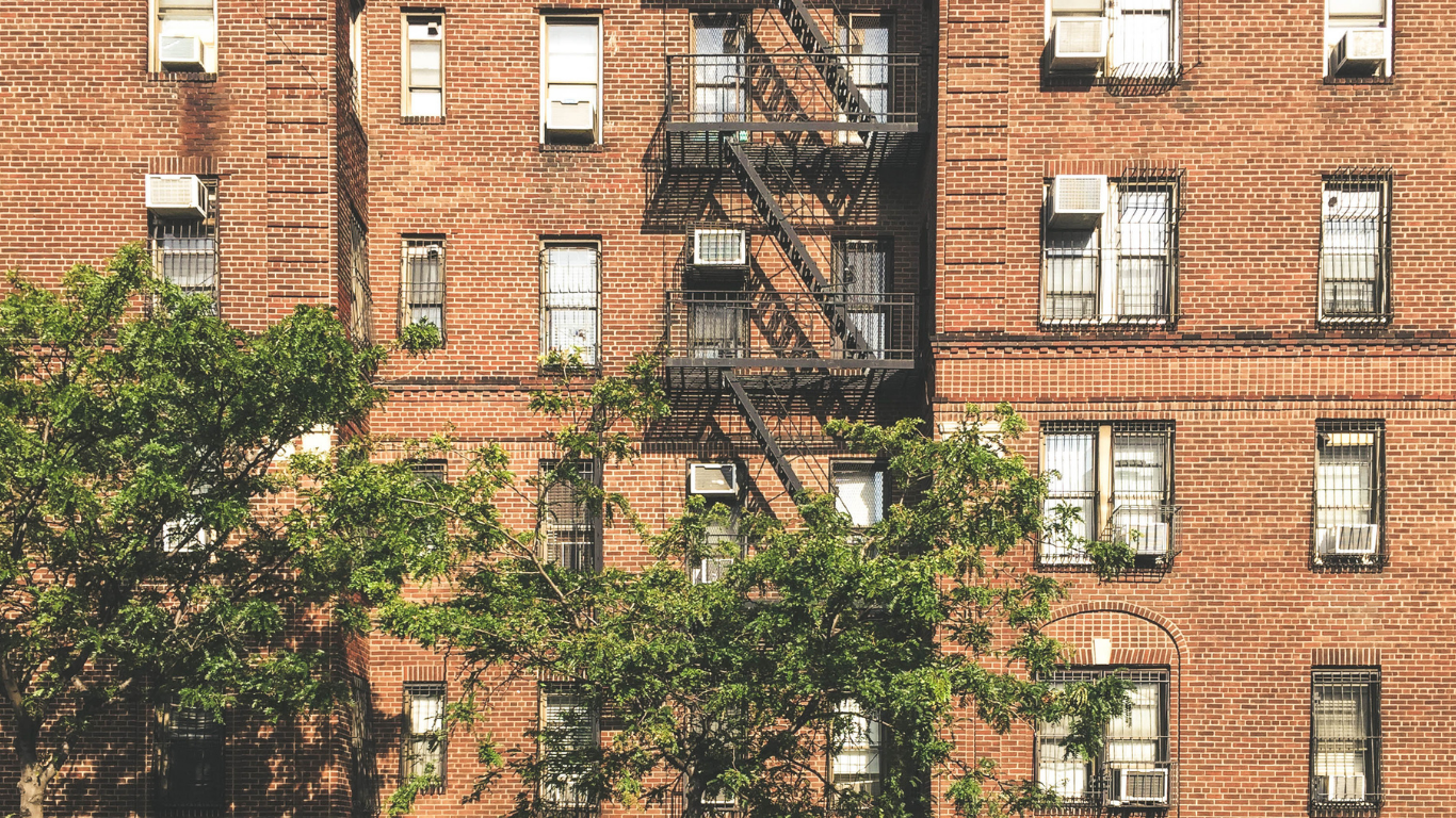 Red brick apartment building with fire escape, trees in foreground.