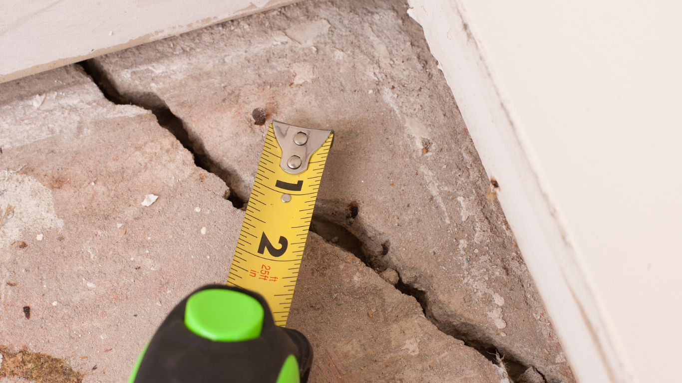 A crack in concrete floor, a tape measure shows the crack is about 1.5 inches wide.