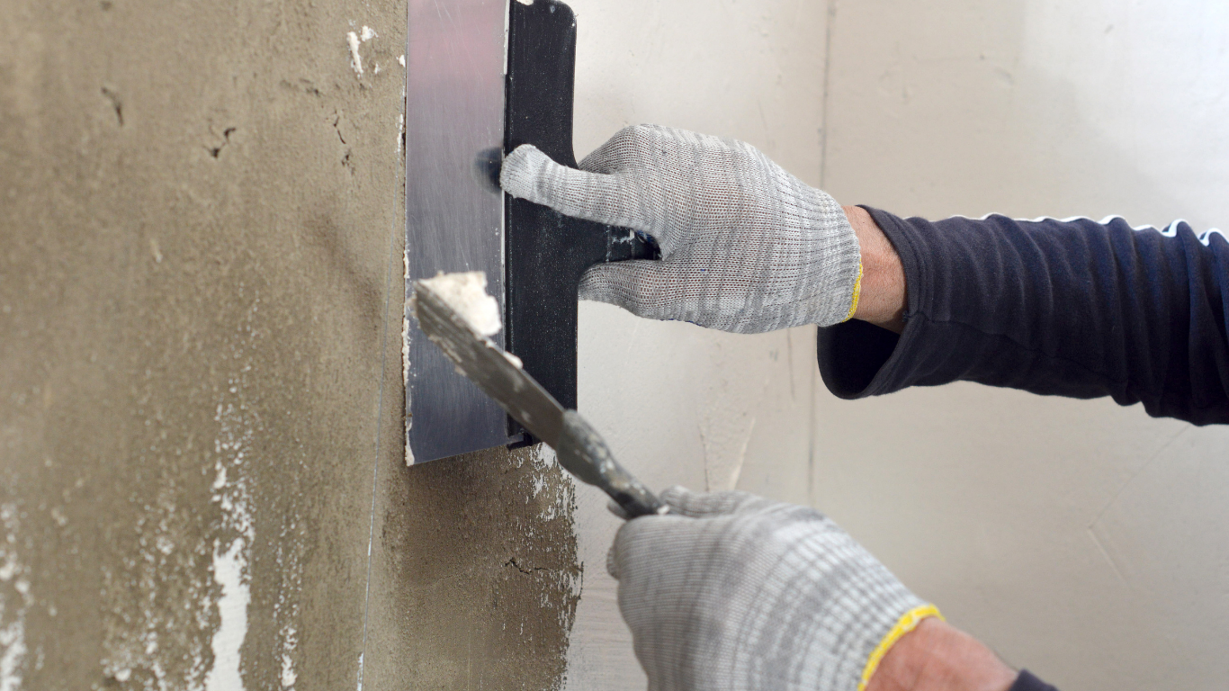 Person using a trowel to apply plaster on a wall, wearing gloves.