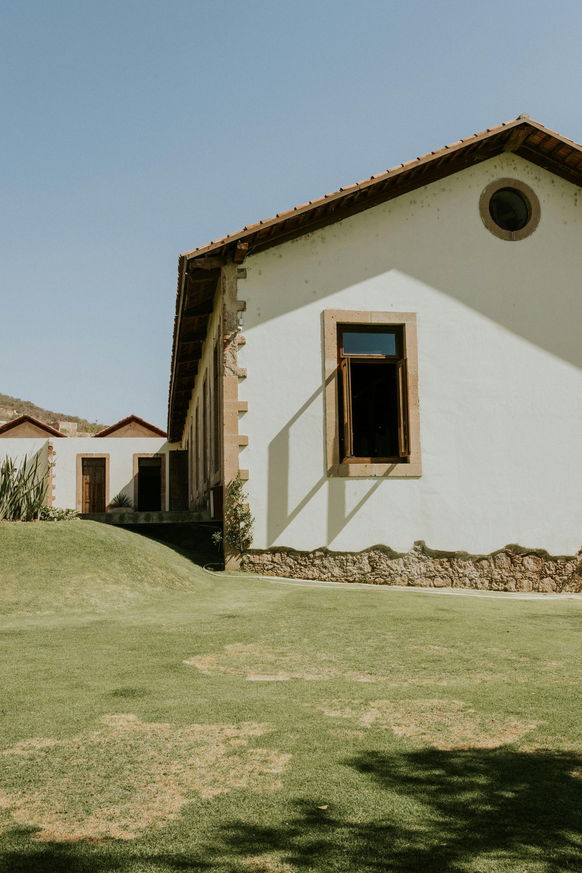 White building with brown trim and open window on a grassy lawn under a clear blue sky.