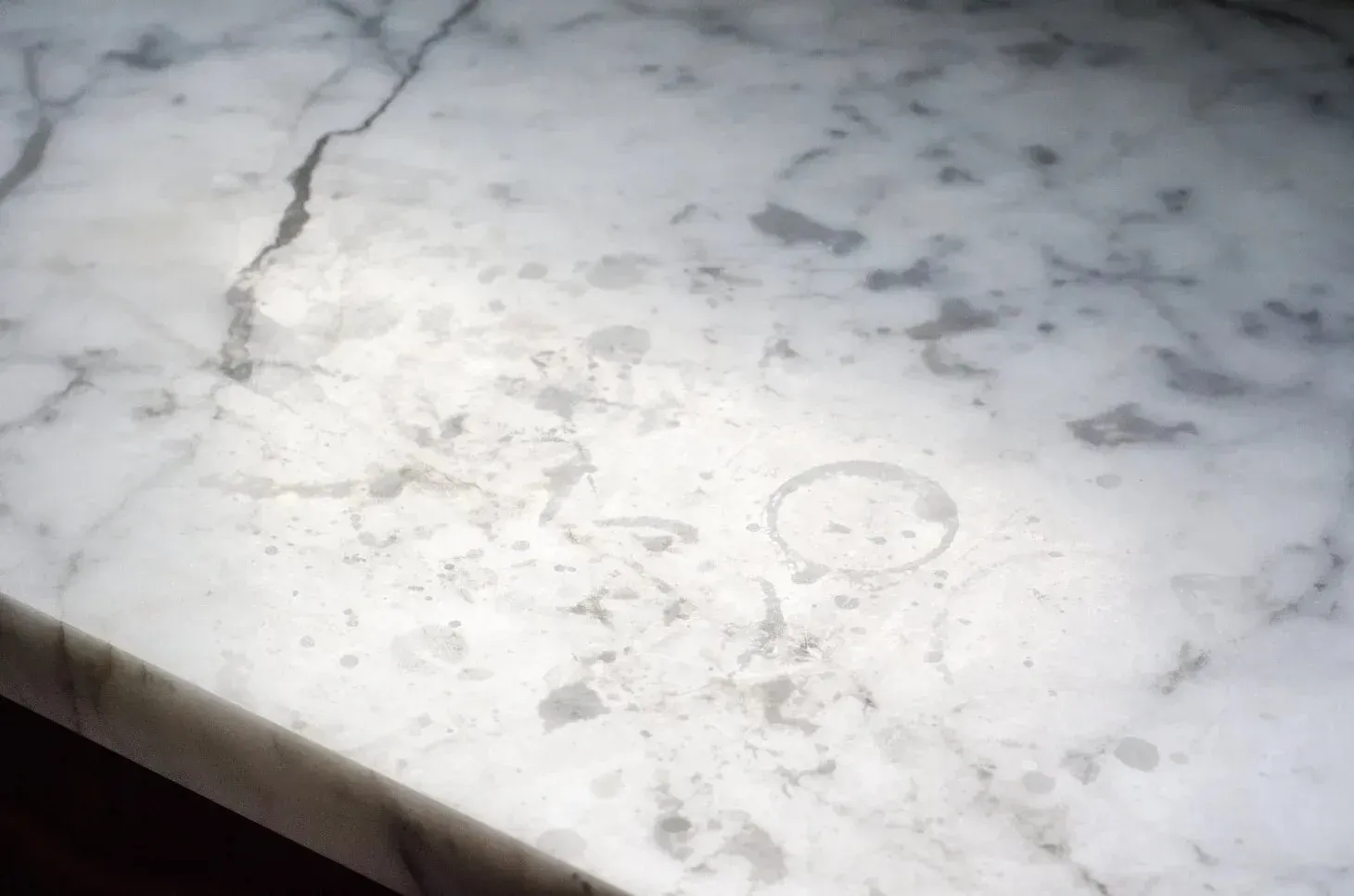 A close up of a white marble counter top with a stain on it.