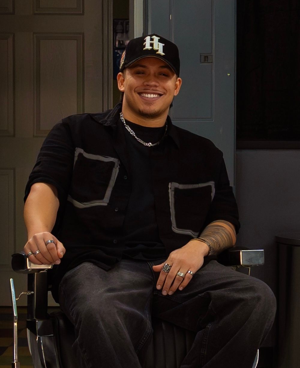 Hairdresser using a comb to cut hair, with tattoos on arms; close-up shot of a person's head.