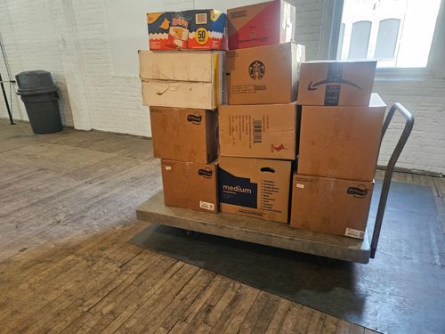 A metal hand truck holding a stack of cardboard boxes in a room.