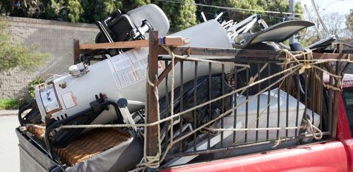 A red pickup truck bed filled with scrap metal, and other appliances, secured with rope.