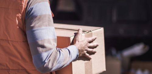 Person carrying a cardboard box outdoors.