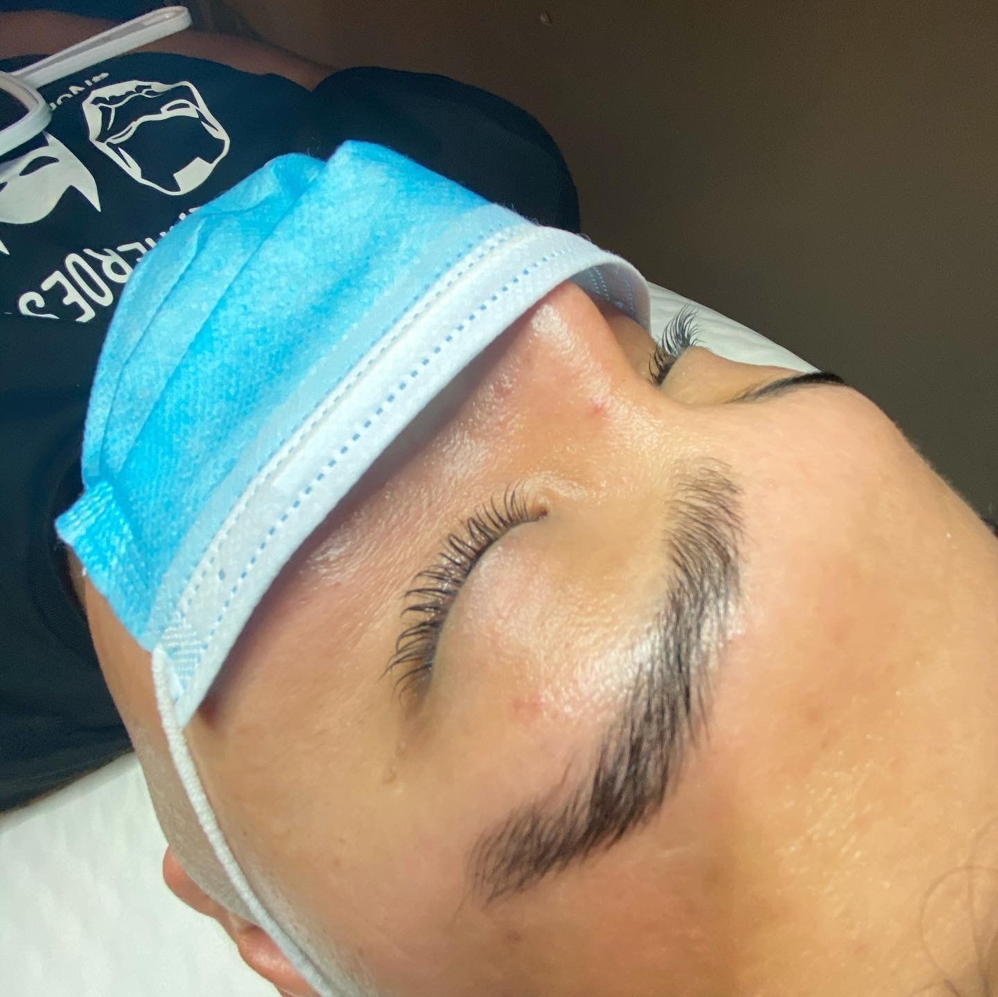 Person lying down with a blue medical mask covering their nose and forehead; eyebrows and eyelashes are visible.