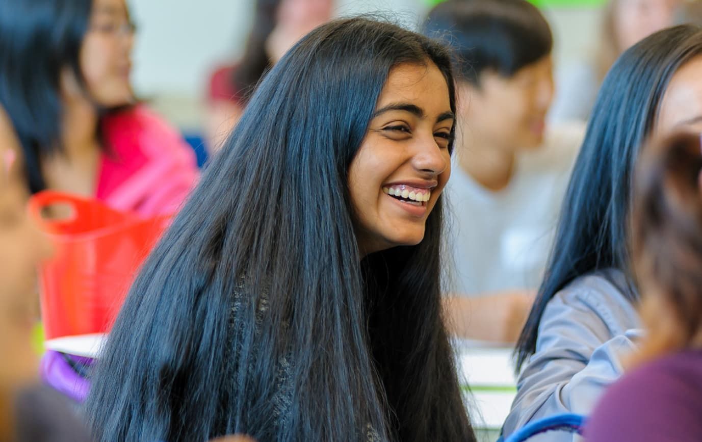 a girl with long black hair is smiling in a classroom