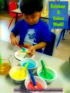 A young boy is sitting at a table with bowls of paint and spoons.