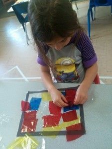 A little girl is sitting at a table playing with colored squares.