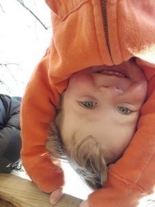 A little boy is hanging upside down on a railing.