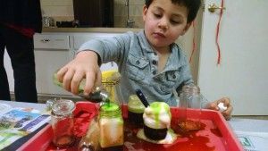 A young boy is pouring liquid into a red tray.