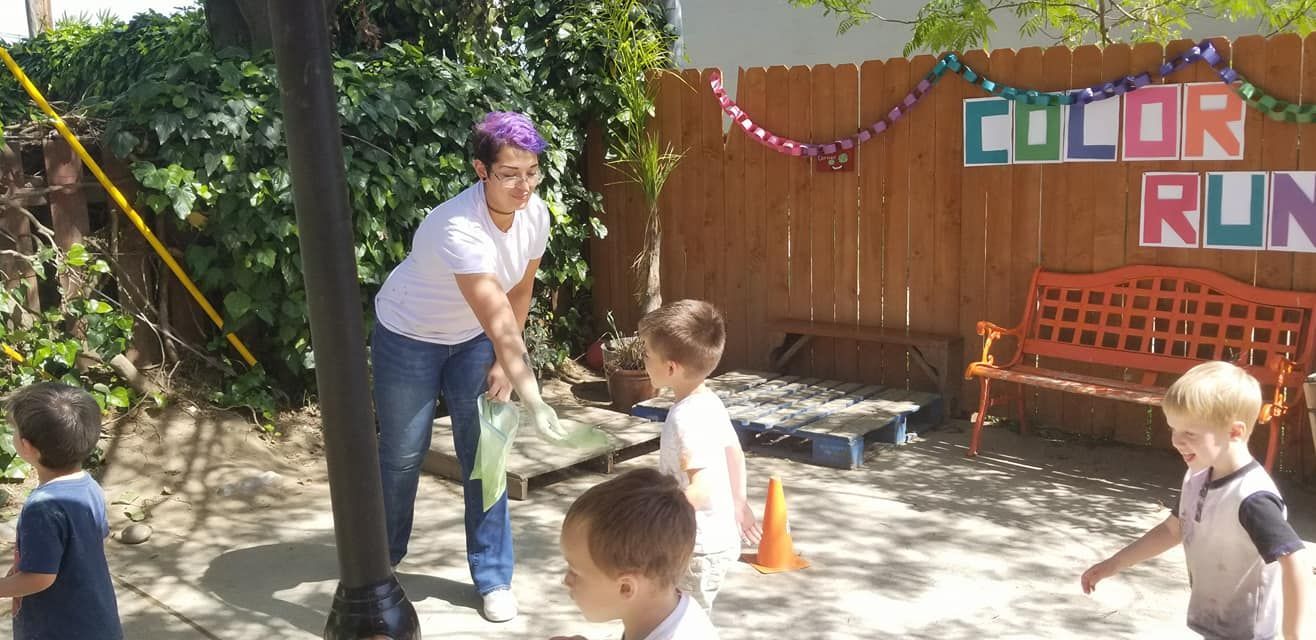 A group of children are playing outside in front of a sign that says color run.