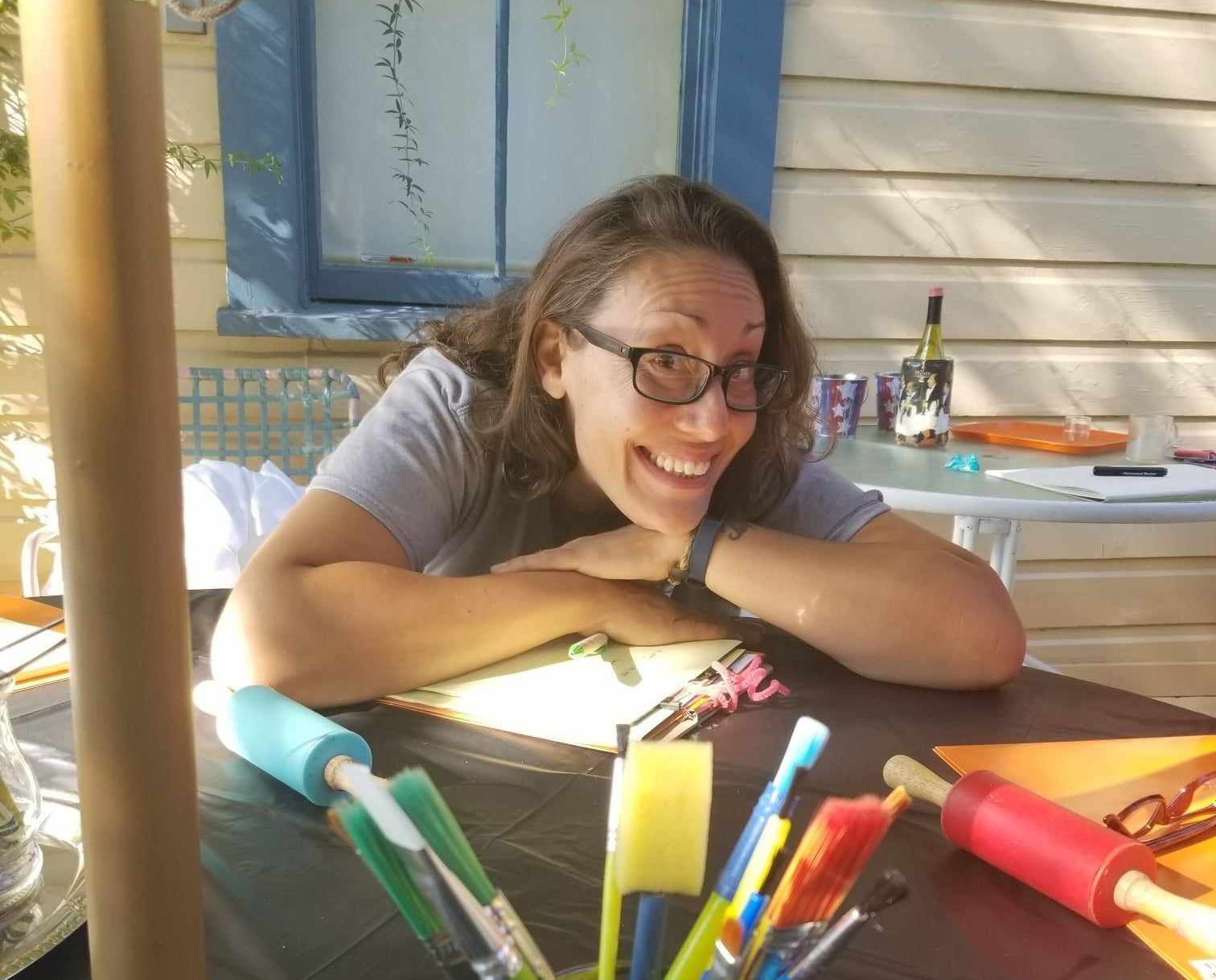 A woman wearing glasses is smiling while sitting at a table