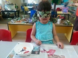 A little girl wearing a mask is painting on a newspaper.