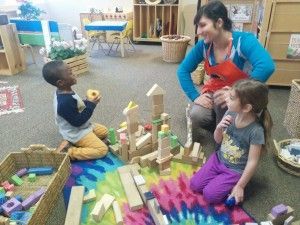 A woman is sitting on the floor with two children playing with wooden blocks.
