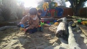 Two children are playing in a sandbox with toys.