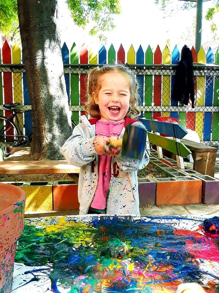 A little girl is playing with paint and a brush