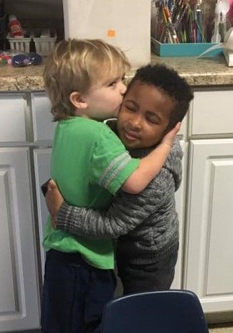 Two young boys are hugging each other in a kitchen.
