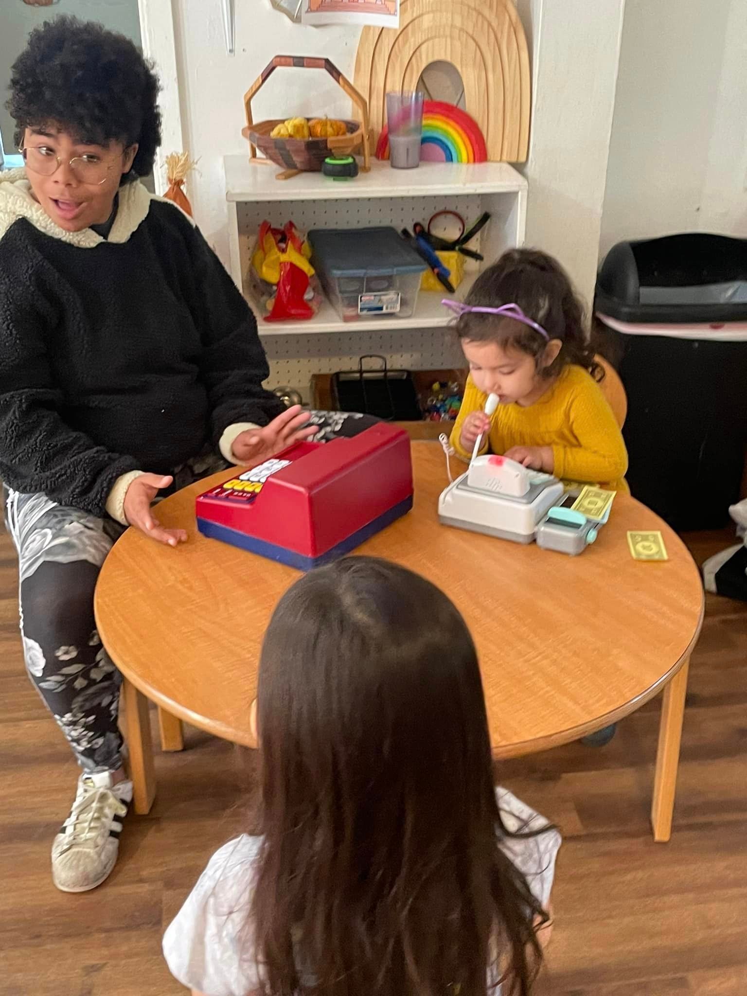 A woman is sitting at a table with two children playing with toys.