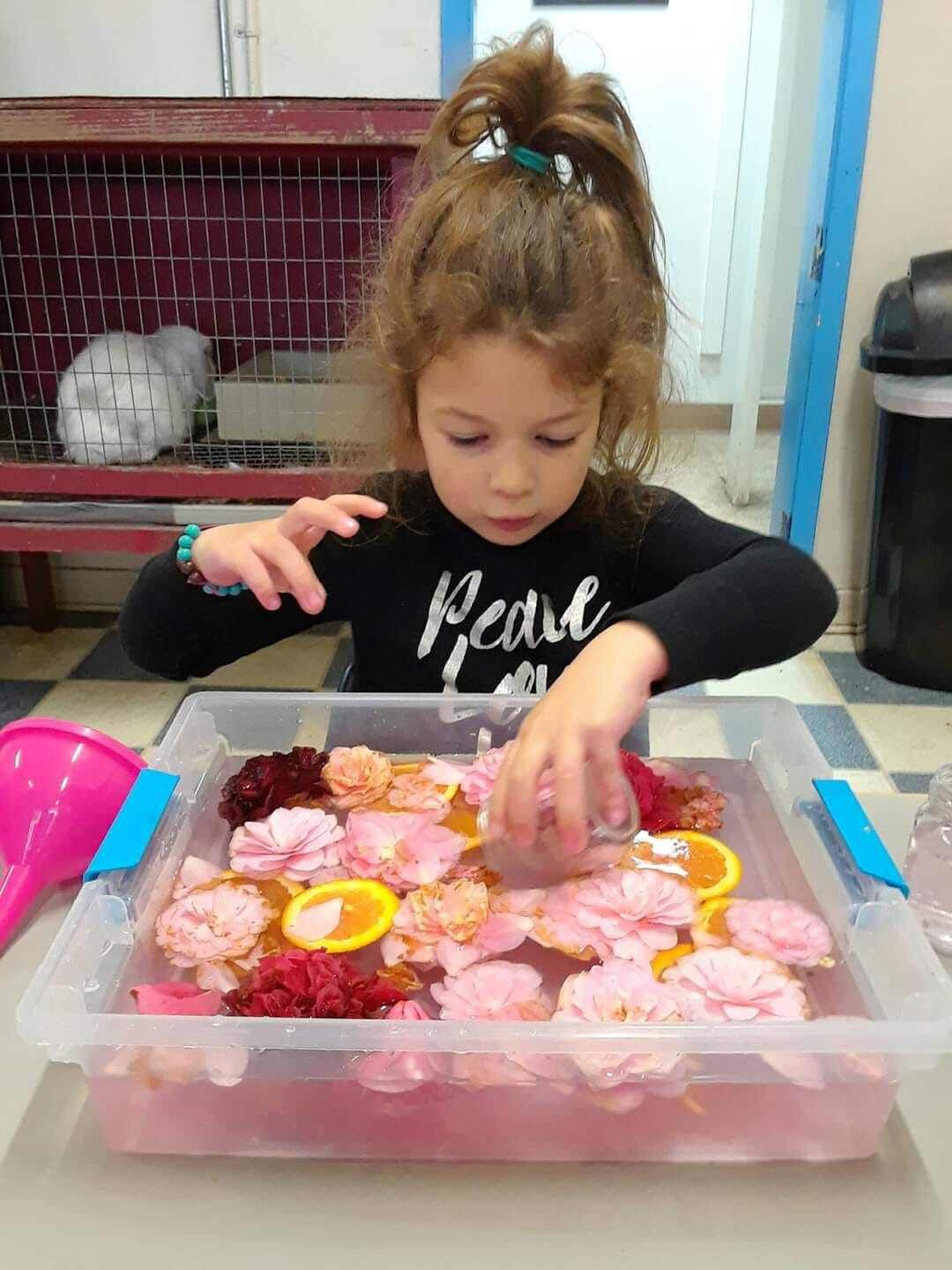 A little girl is playing with flowers in a plastic container.