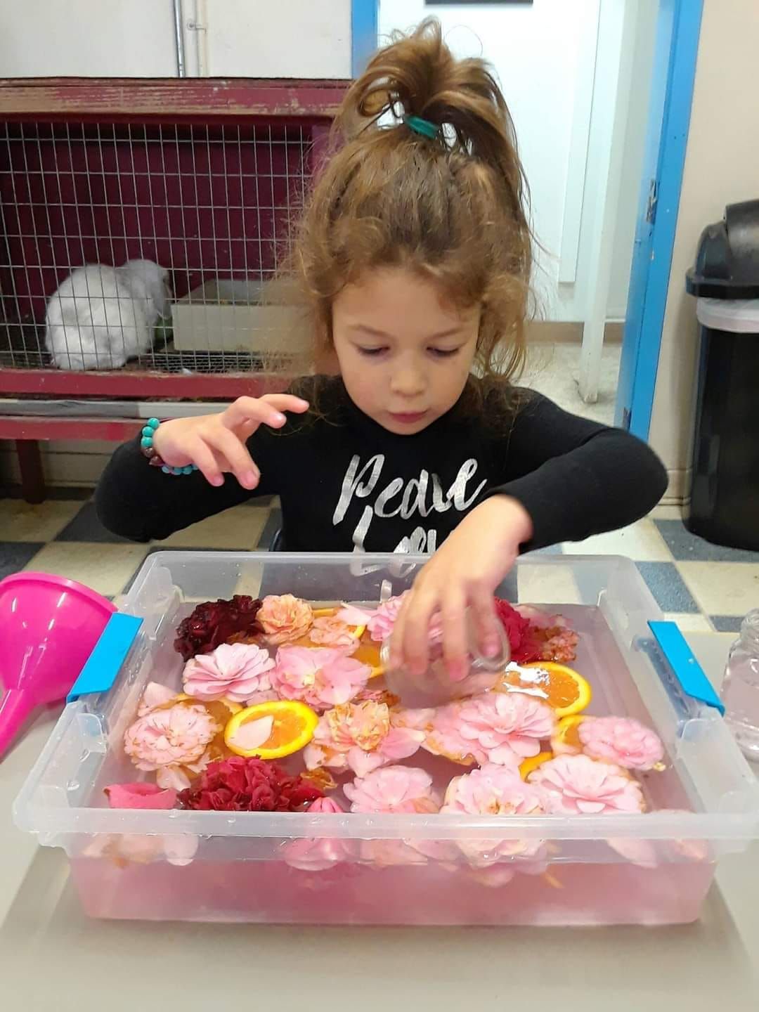 A little girl is playing with flowers in a plastic container.