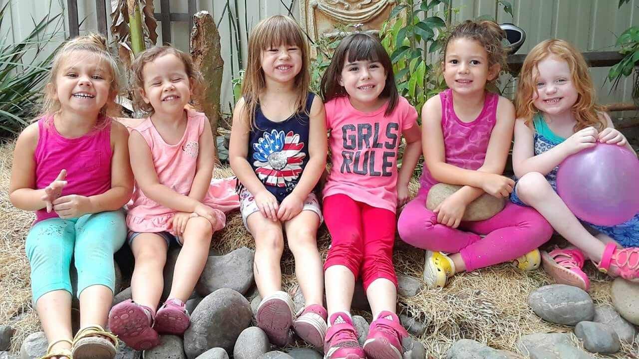 A group of young girls are sitting on rocks with one girl wearing a shirt that says girls rule