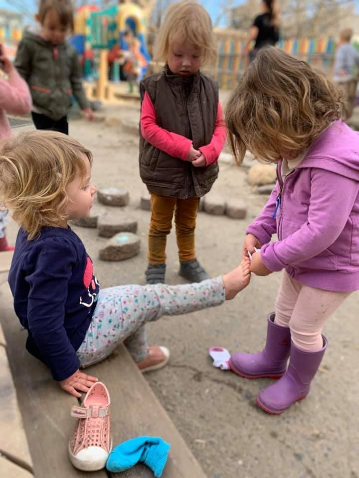 Two little girls are sitting on a bench playing with their feet.