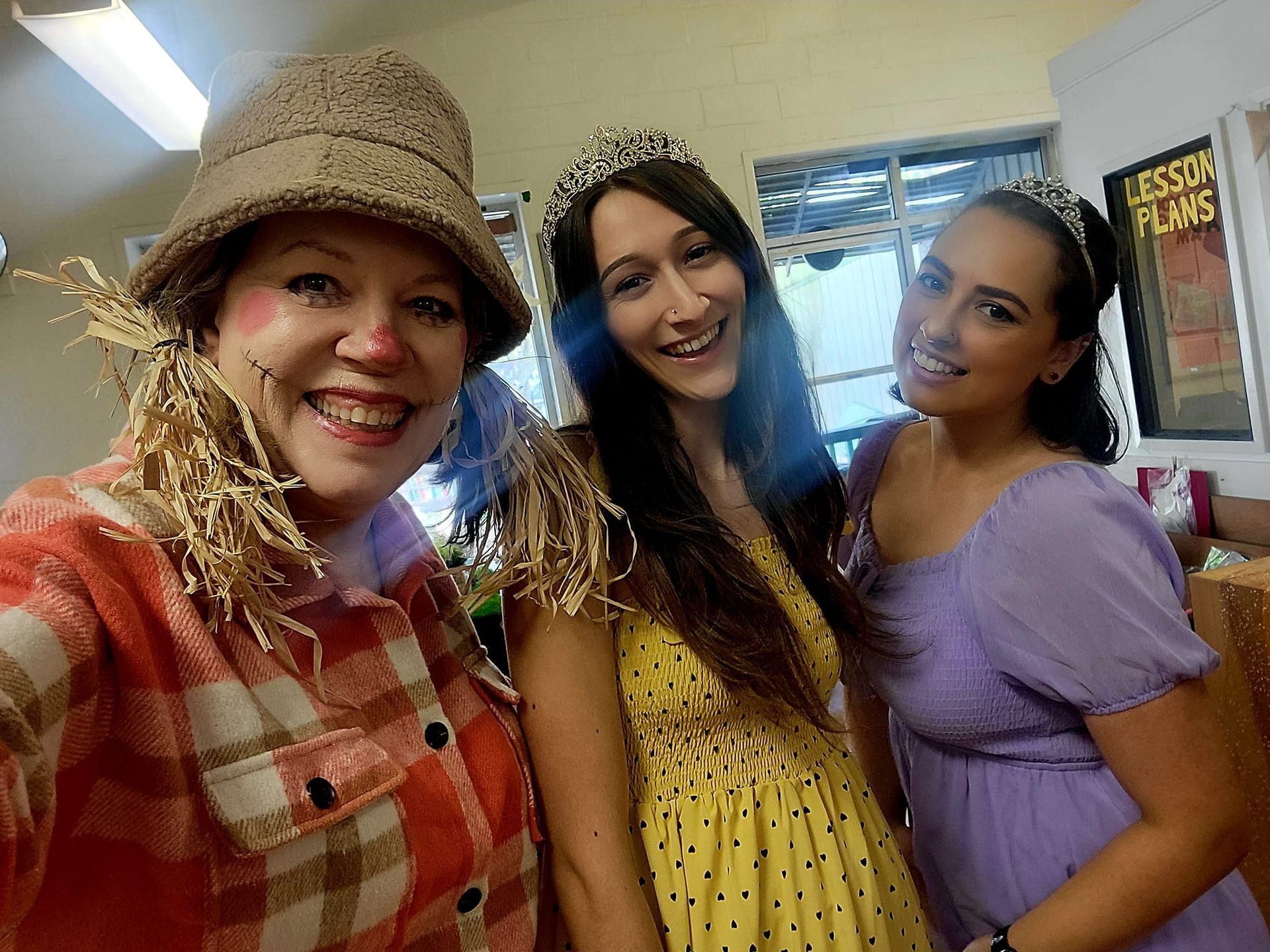 Three women are posing for a picture and one is dressed as a scarecrow