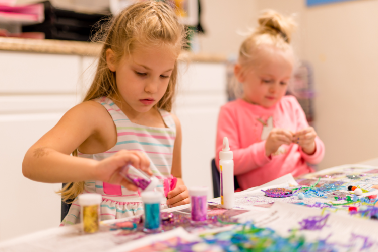 Two little girls are sitting at a table playing with glitter.