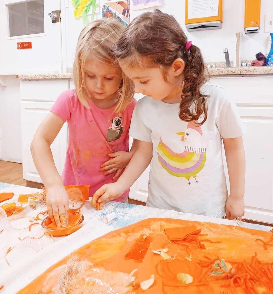 Two little girls are playing with orange paint on a table.