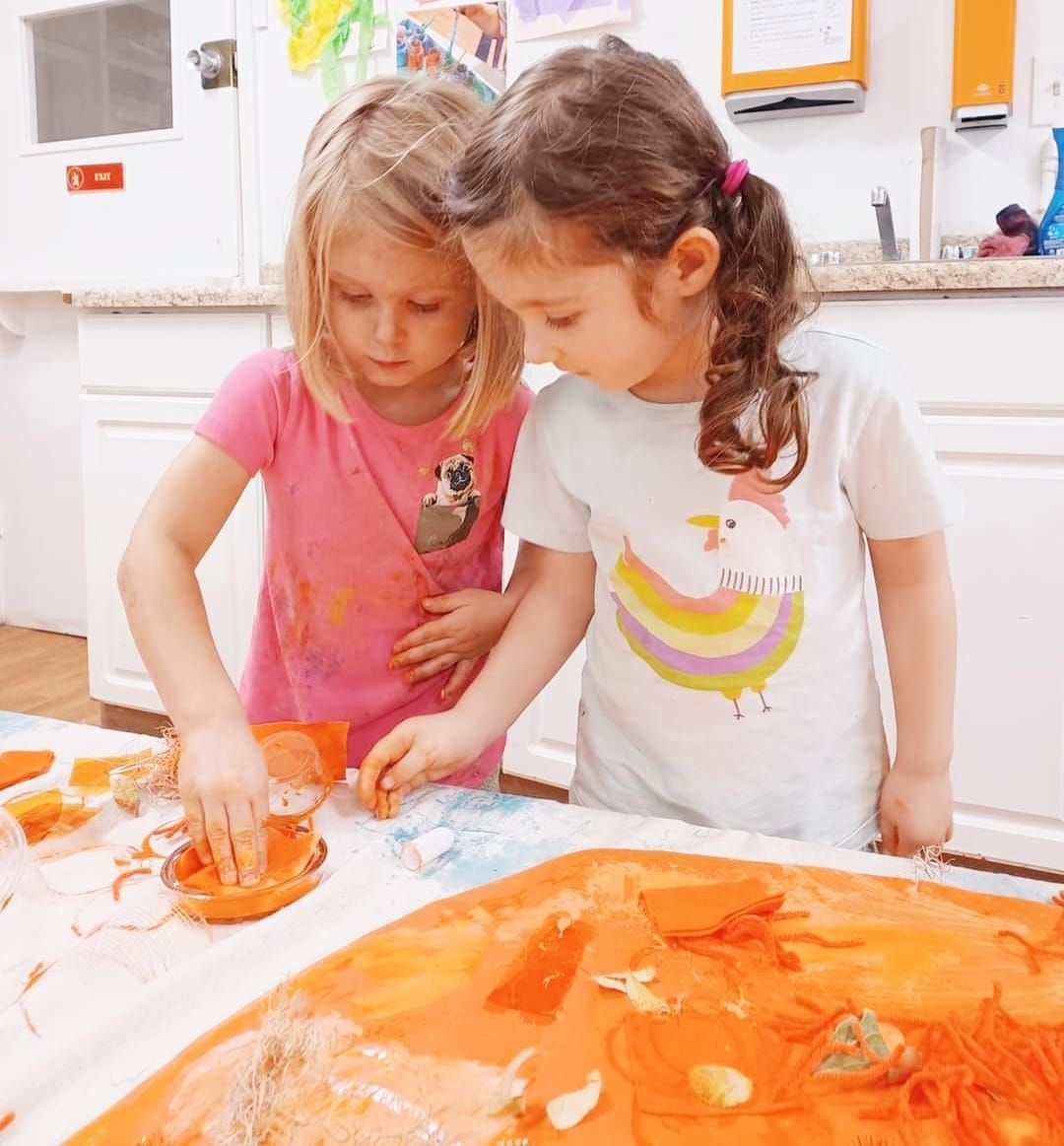 Two little girls are playing with food on a table.