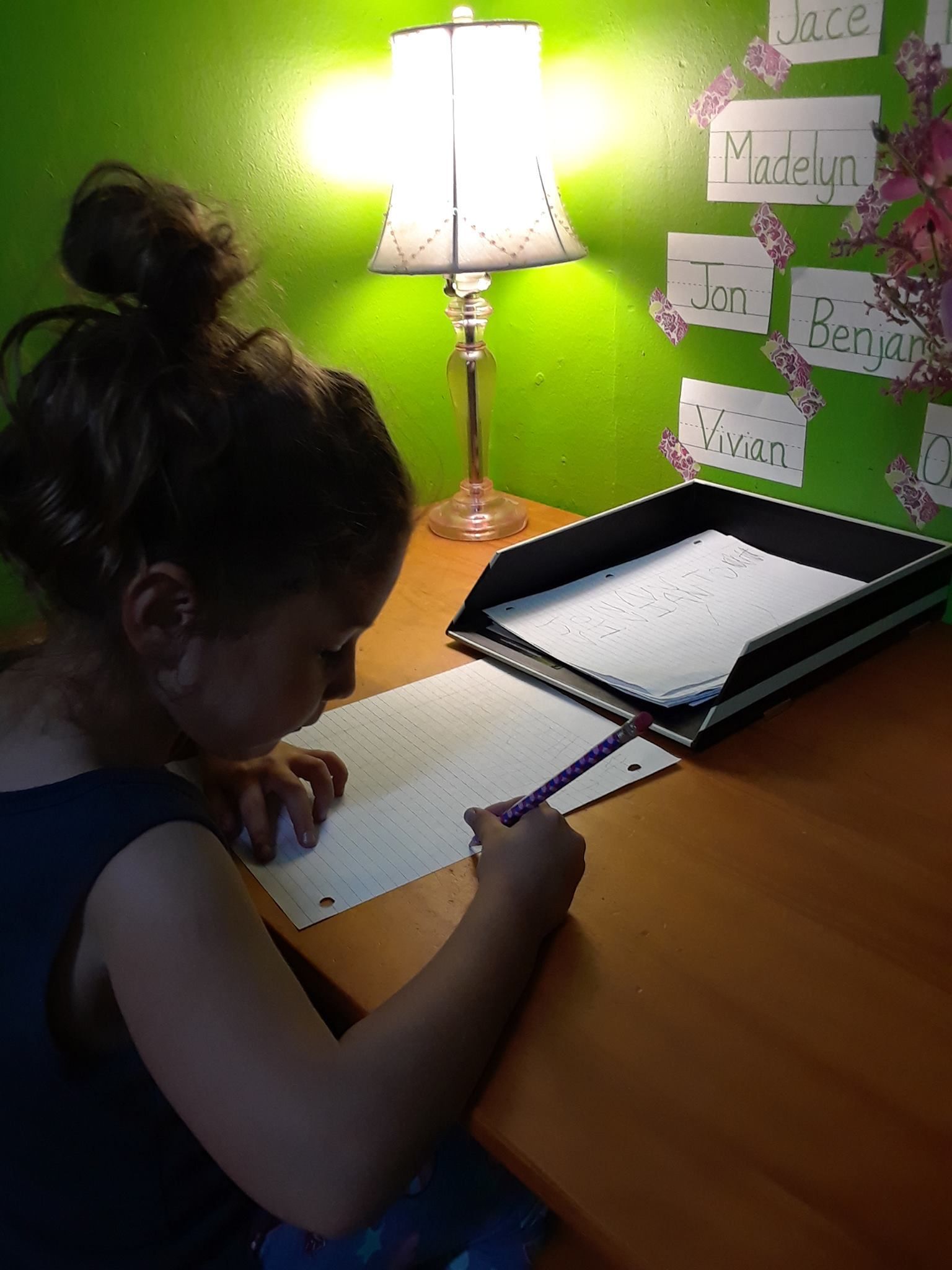 A little girl is sitting at a desk writing on a piece of paper