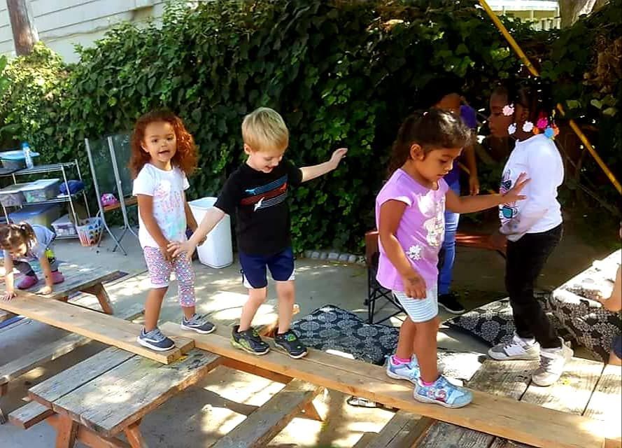 A group of children are standing on a wooden balance beam.