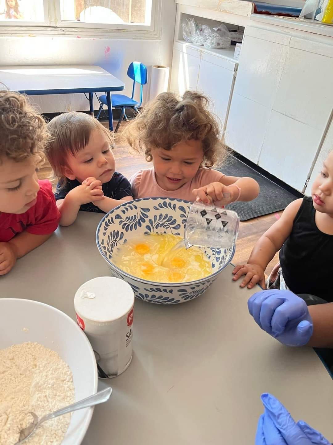 A group of children are sitting at a table mixing ingredients in a bowl.