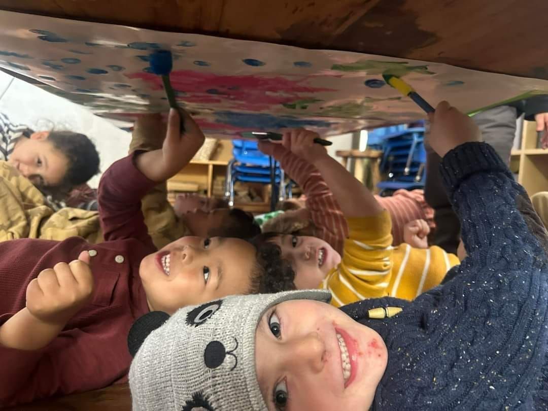A group of children are painting on a cardboard box