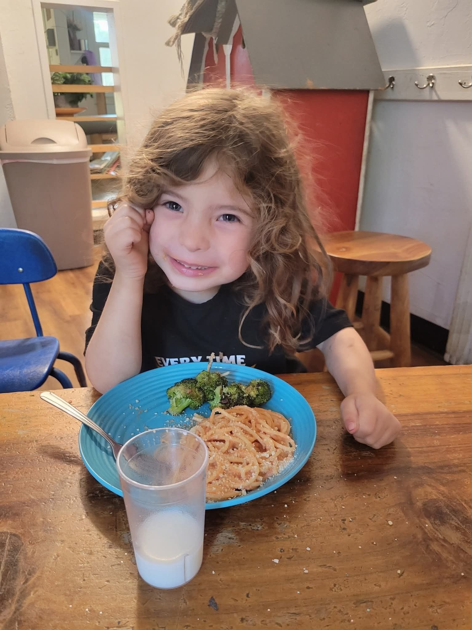 A little girl is sitting at a table with a plate of food and a glass of milk.