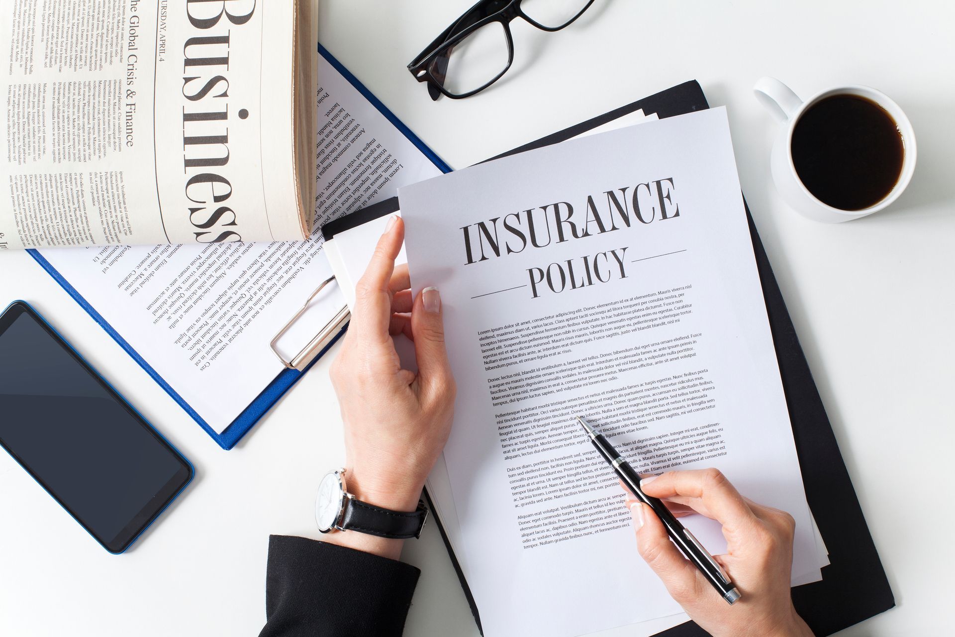 Person reviewing an insurance policy document at a desk with coffee, glasses, and a newspaper.