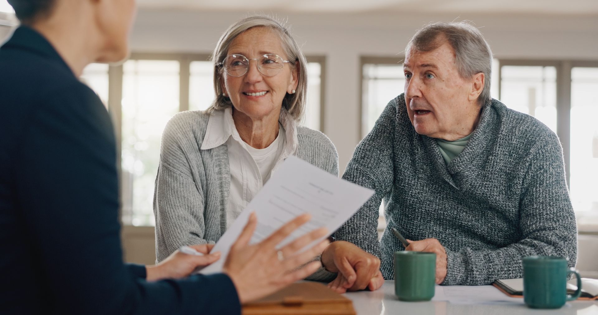 A financial advisor reviewing documents with a senior couple at a table; they are seated in a home setting.
