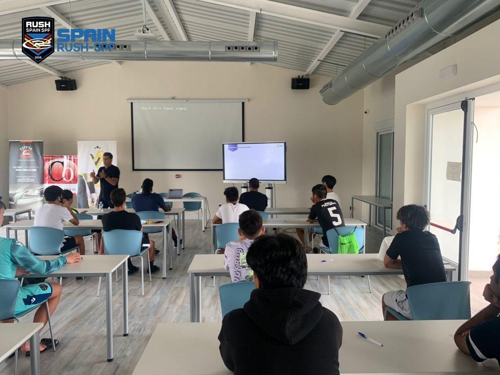 A group of student athletes sitting at tables in front of a projector screen.