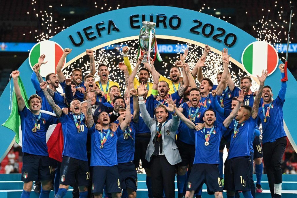 Italy Men's National Soccer Team holding up the UEFA Euror trophy in front of a sign that says UEFA Euro 2020