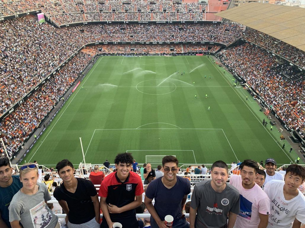 A group of young men are standing in front of a soccer stadium.