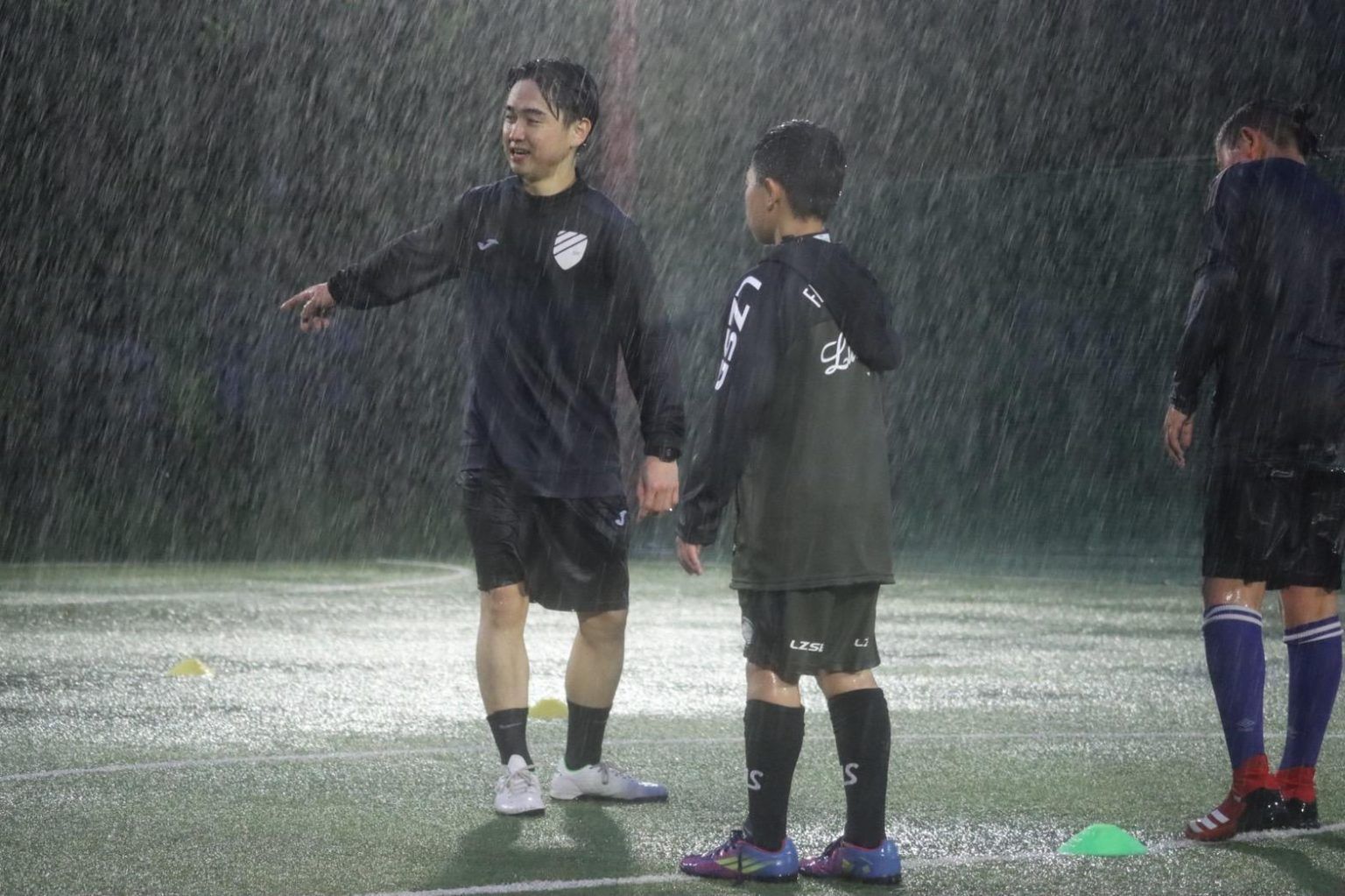 A group of people are standing on a soccer field in the rain.